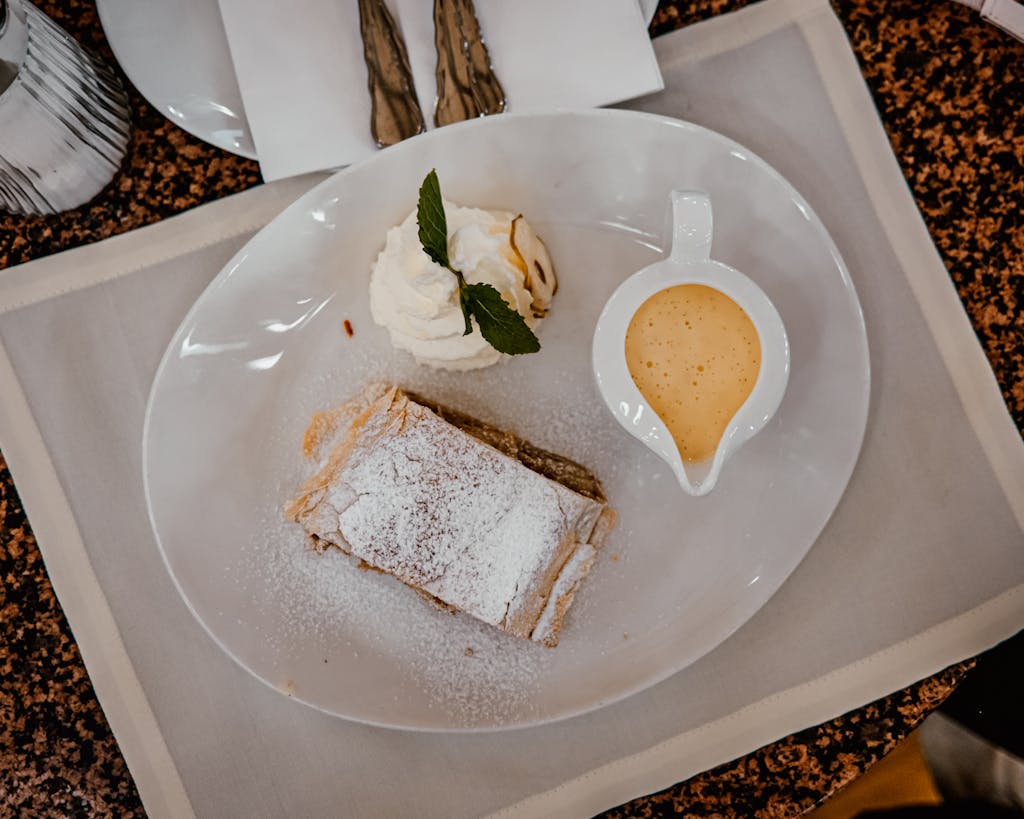 Delicious apple strudel served with whipped cream and vanilla sauce on a white plate.