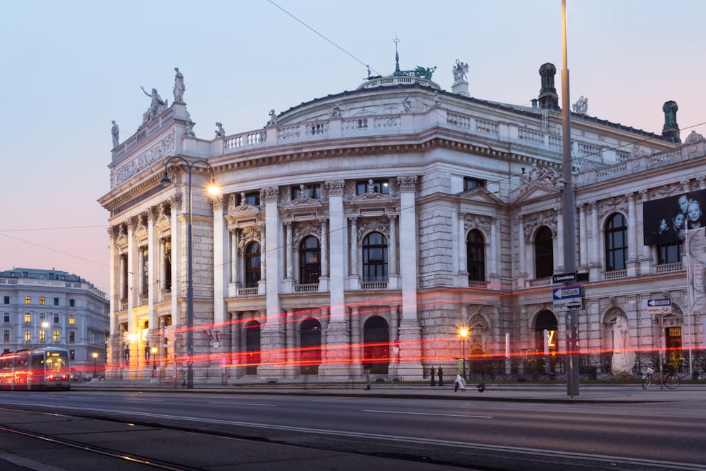 Evening view of Vienna's Burgtheater with light trails and Baroque architecture.