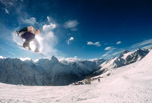 Snowboarder performing a high jump in a picturesque snow-covered mountain landscape during the day.