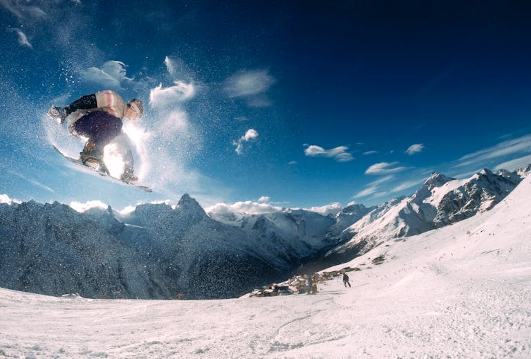 Snowboarder performing a high jump in a picturesque snow-covered mountain landscape during the day.