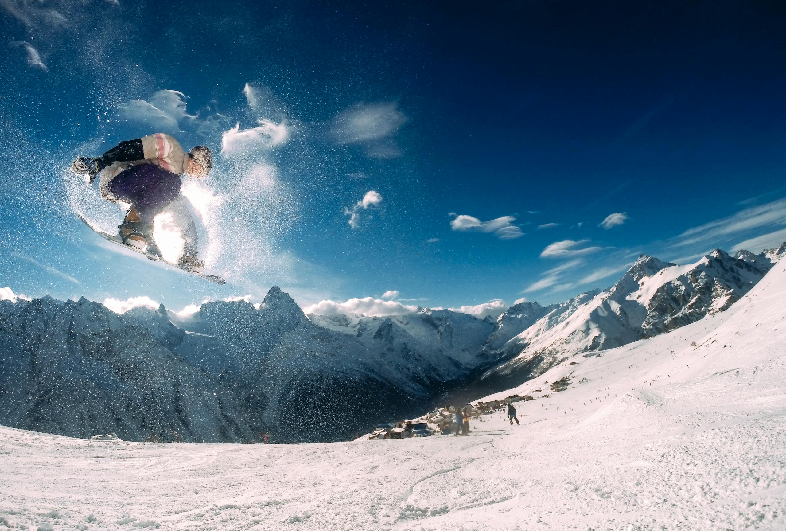 Snowboarder performing a high jump in a picturesque snow-covered mountain landscape during the day.