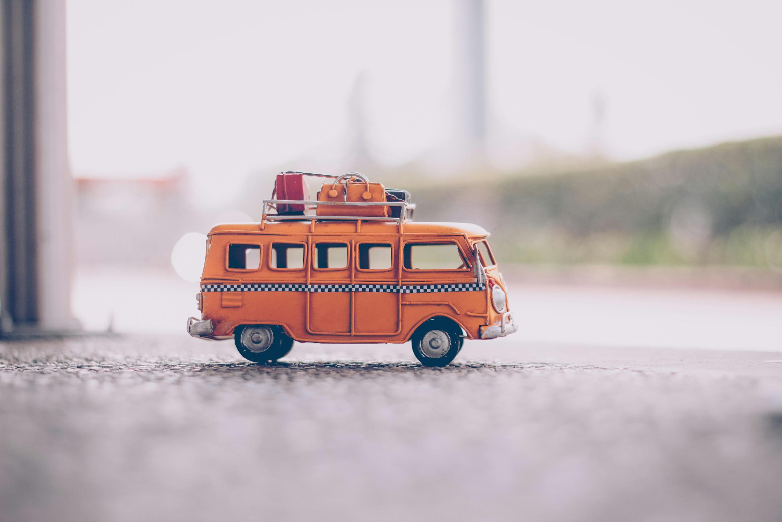 Close-up of a vintage orange toy van with luggage on a textured surface, capturing a nostalgic travel vibe.