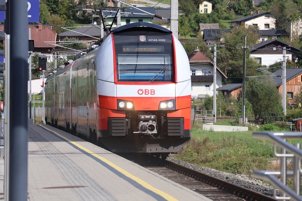 ÖBB train approaching a rural station in Austria, showcasing scenic village views.